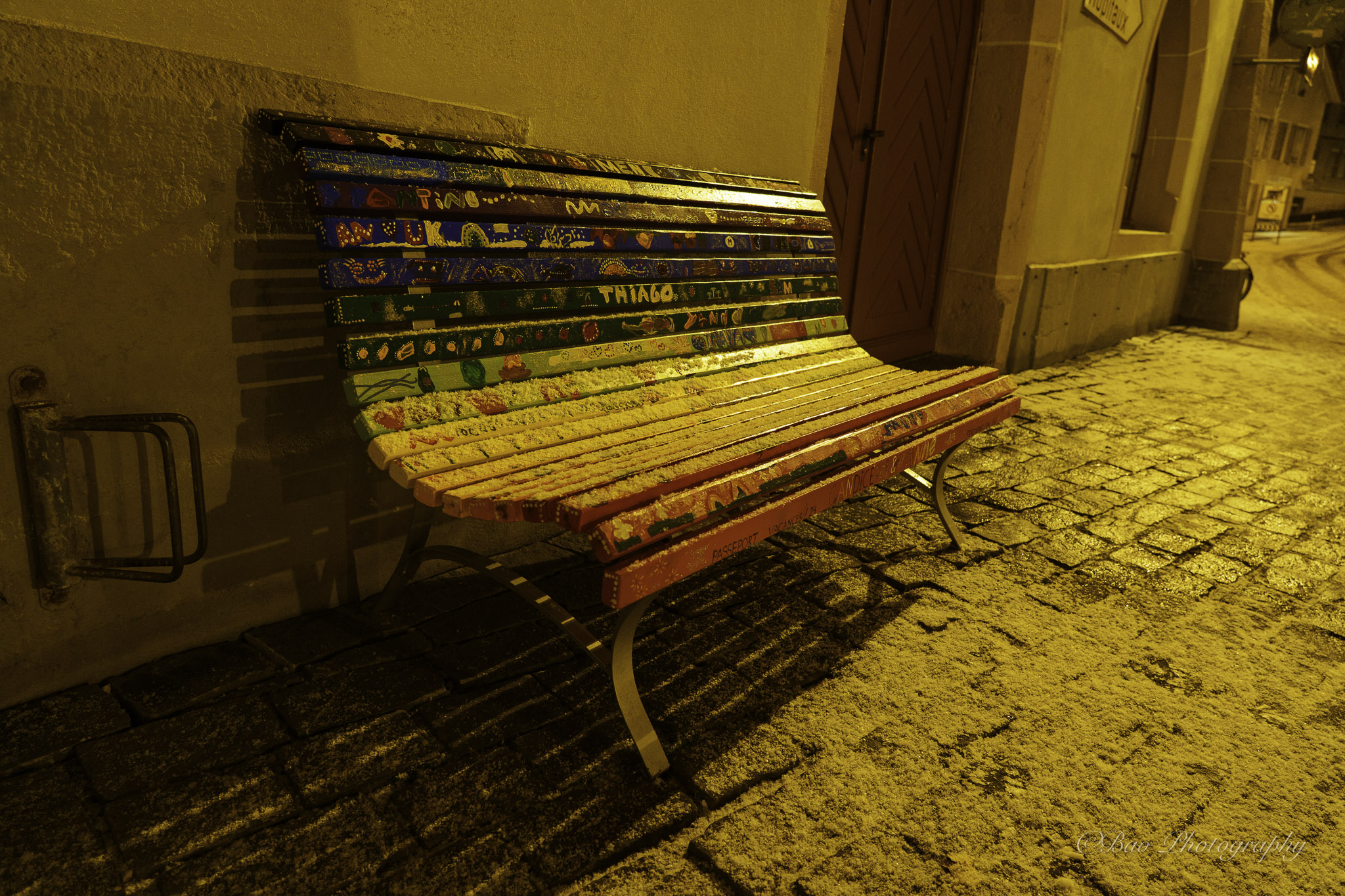 Colorfully decorated wooden bench on a cobblestone street in Biel old town at night