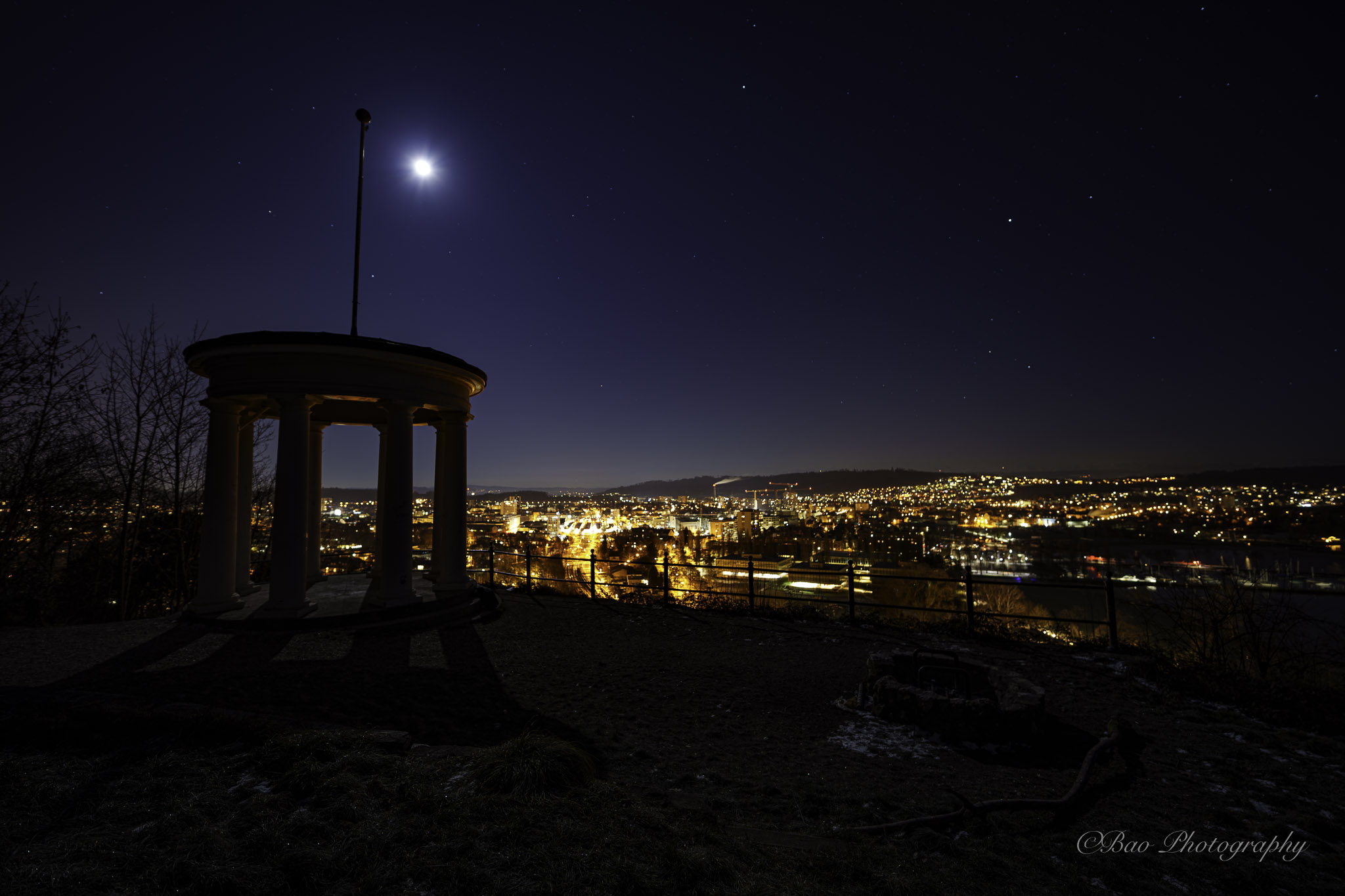 Pavillon Felseneck silhouette under moonlight with the city of Biel illuminated below at night