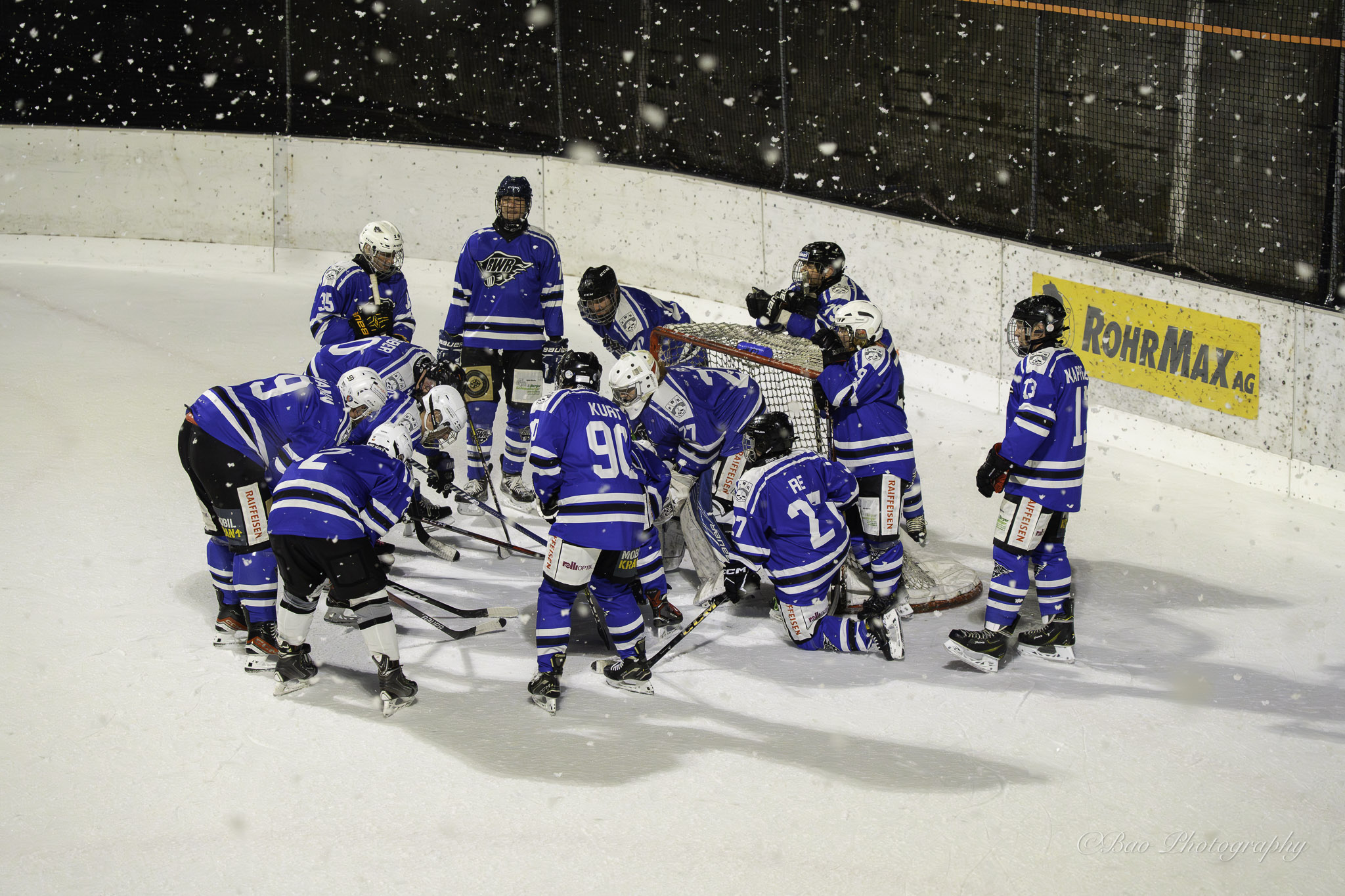 Blackwater Rangers ice hockey team huddling near the goal on an outdoor rink during snowfall