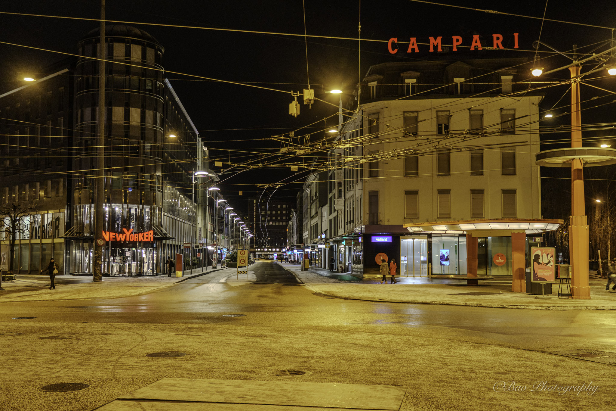 Empty Zentralplatz in Biel at night with trolleybus wires and illuminated buildings on wet pavement